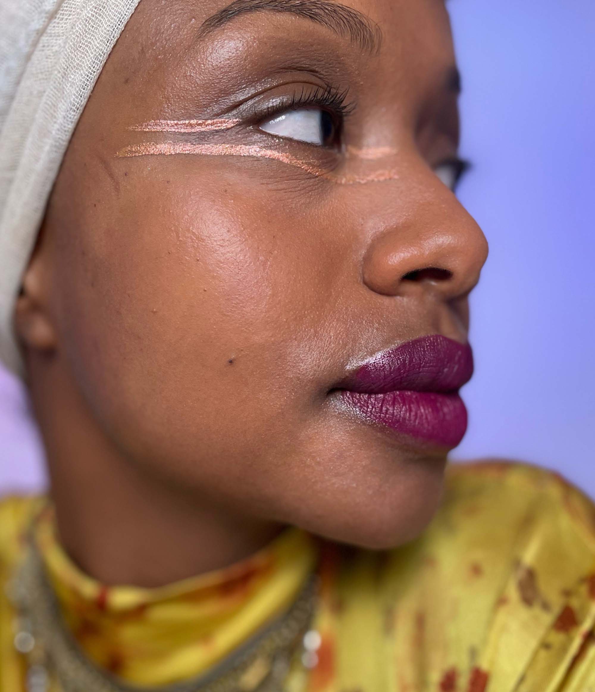 Side view of Model with dark skin tone with Deepdive colorpot in Eventide in lines across their eye area.