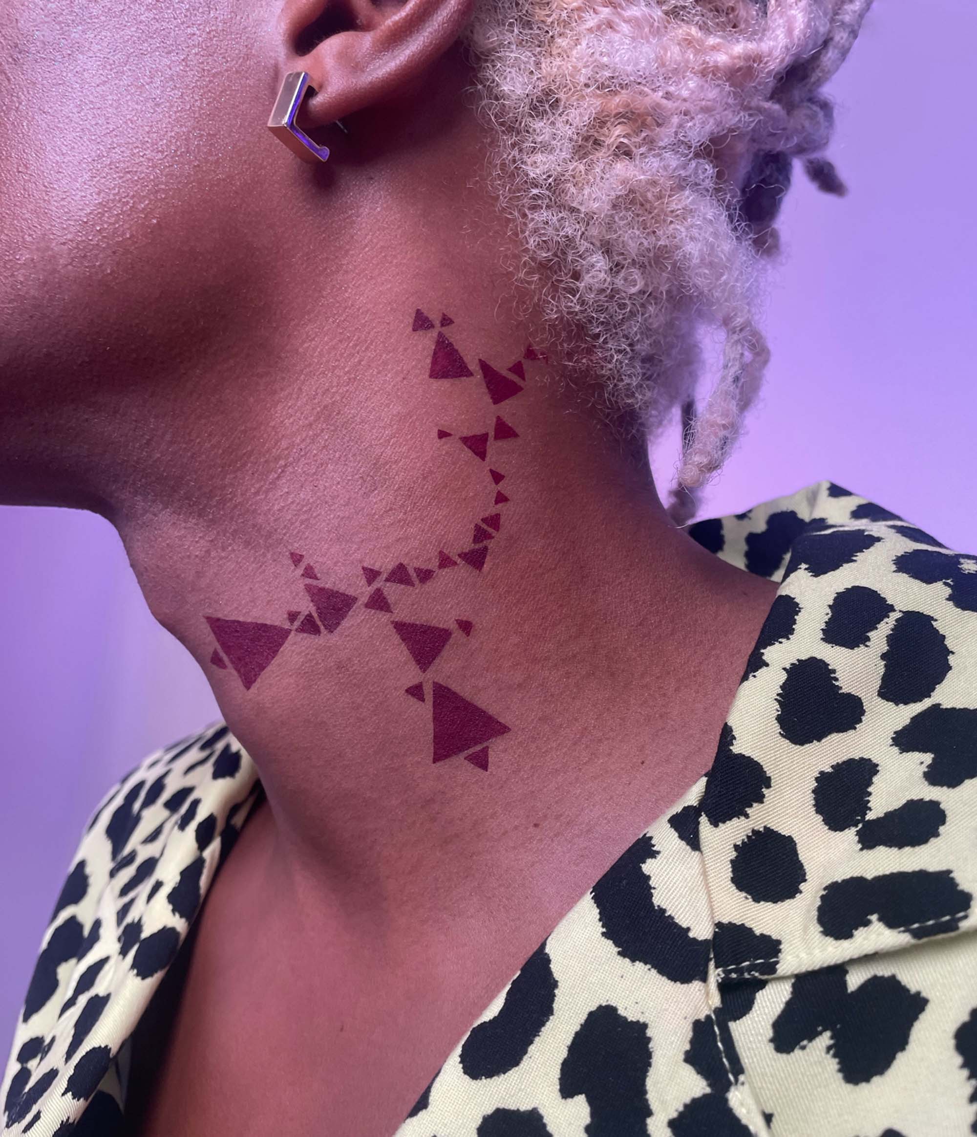 Side view of Model with dark skin tone with Deepdive colorpot in aeonium in a triangle pattern from stencils along the side of their neck.